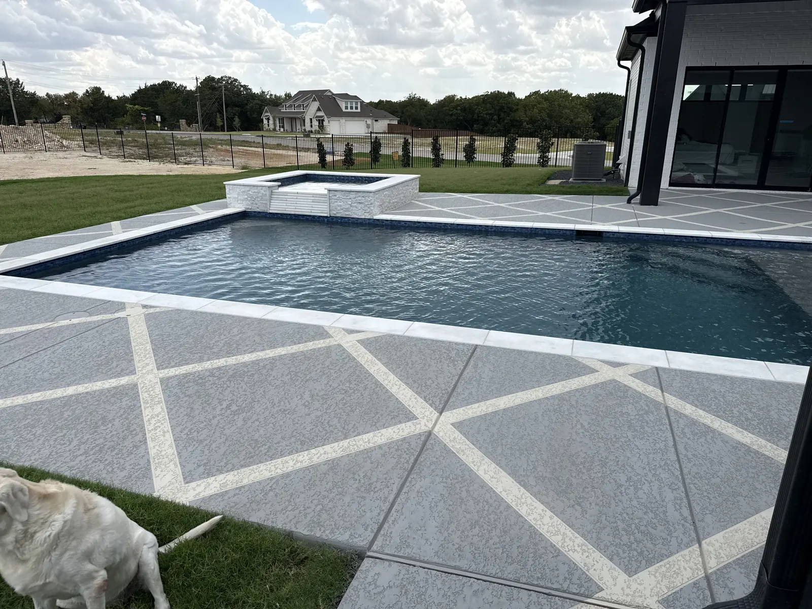 Gray Sundek pool deck with cream geometric bands beside a raised spa and covered patio