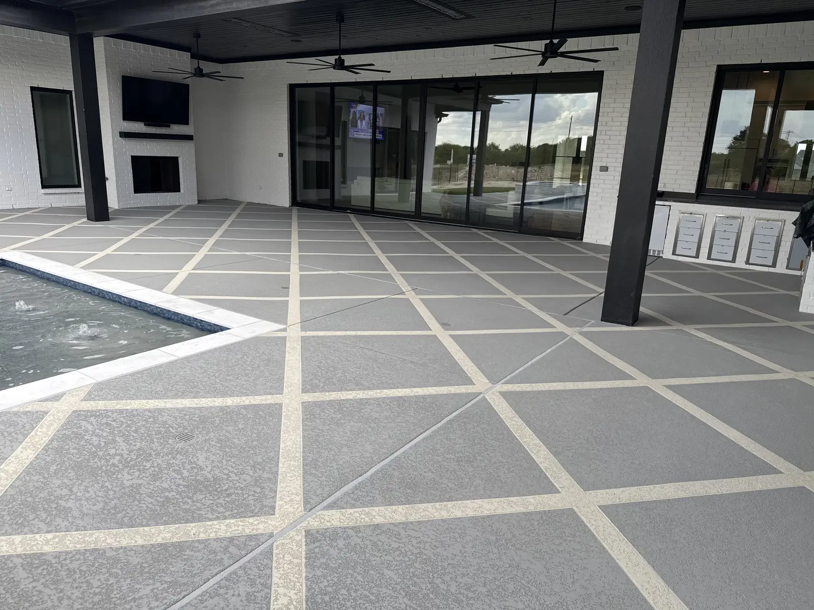 Sundek overlay extending from the pool edge across a covered outdoor living area