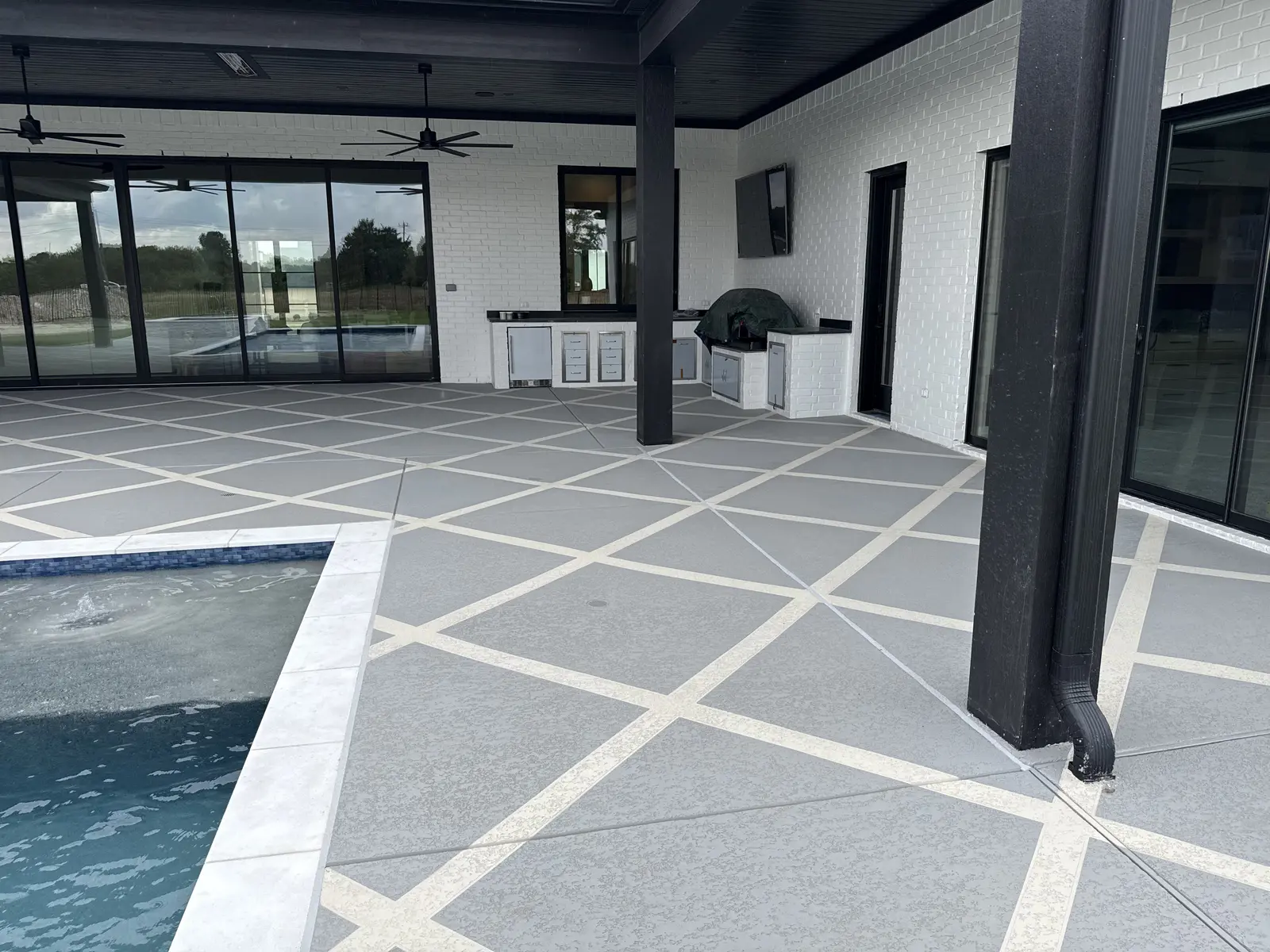 Finished Sundek overlay surrounding the pool coping, patio columns, and outdoor kitchen