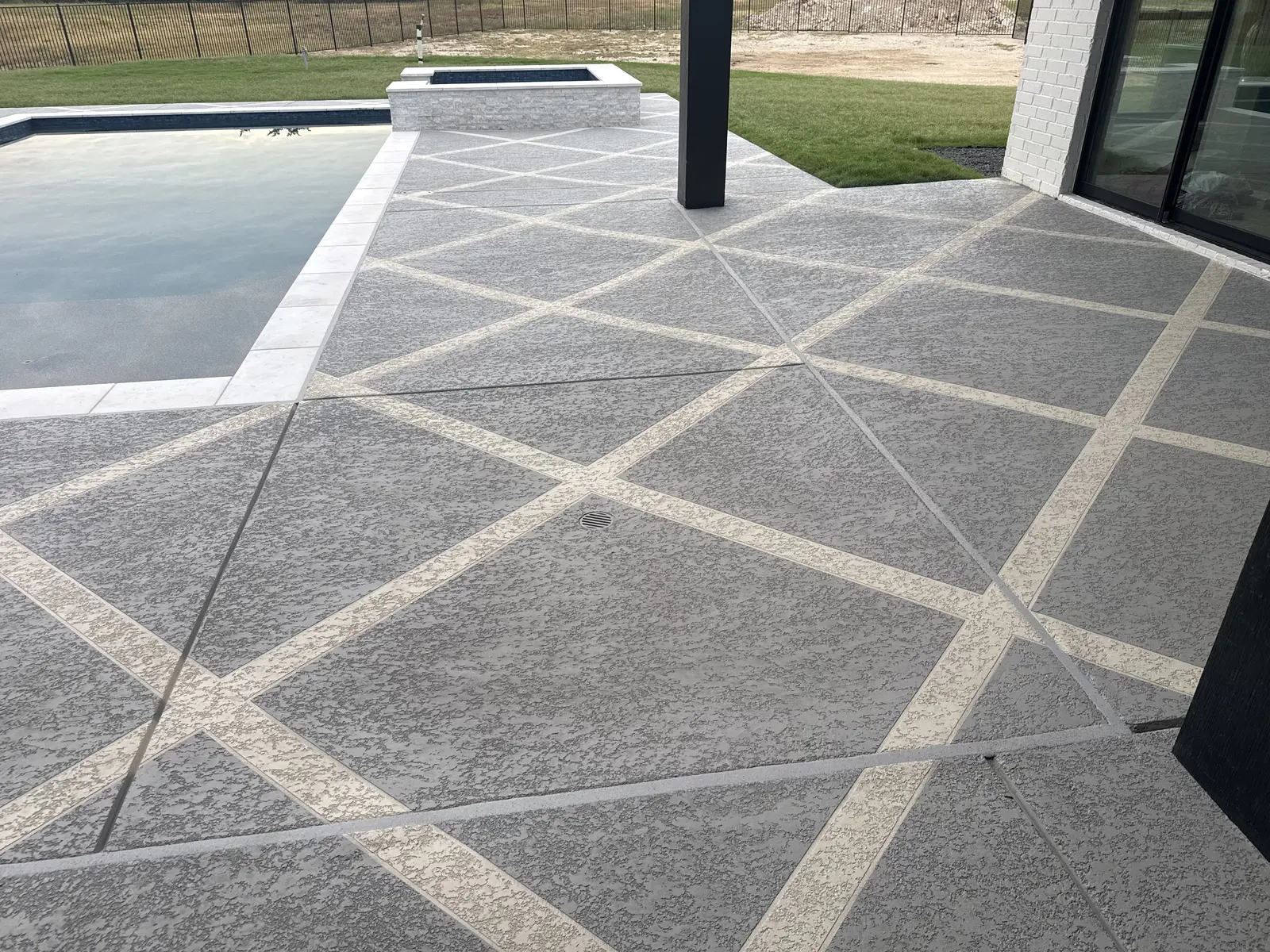 Close view of textured gray Sundek coating and intersecting cream accent bands beside the pool