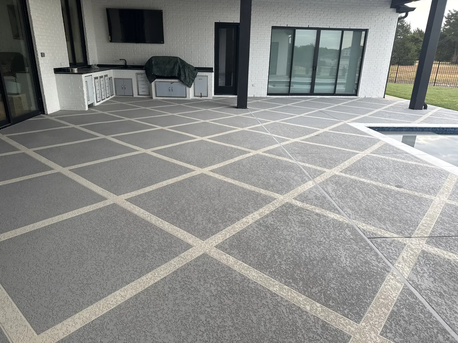 Wide view of Sundek overlay beneath a covered patio with an outdoor kitchen and pool