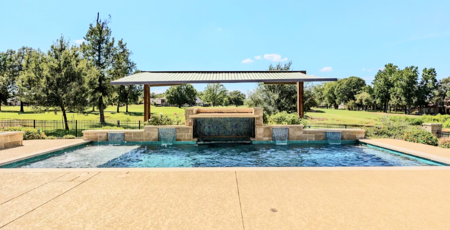 A view across the new swimming pool toward the raised beam wall, grotto, and cedar arch.